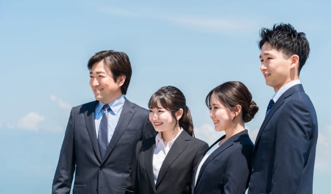 青空の下で並ぶスーツ姿の社員たち